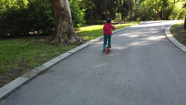 Happy little boy riding a scooter in the park. 4k video of boy riding kick scooter.