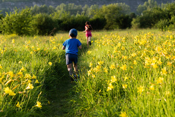 Cute  little boy and girl running in field with beautiful yellow flowers  summer. Happy childhood concept.