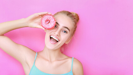 Girl with a donut on a pink isolated background.  Face with a smile of a beautiful blonde girl who is holding a pink night lamp near her face.  Copy space.