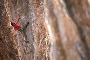 A strong man climbs a beautiful orange rock.