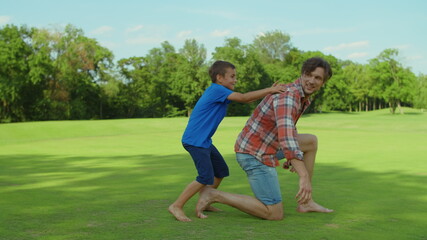 Man and boy playing in meadow. Father giving son piggyback riding outdoors