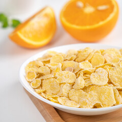 Corn flakes bowl sweeties with milk and orange on white background, close up, fresh and healthy breakfast design concept.