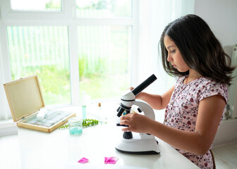 Pretty blonde little girl working with test tube and microscope. The kid learning science in the school laboratory or at home. Child looking make experiment with microscope on the table.