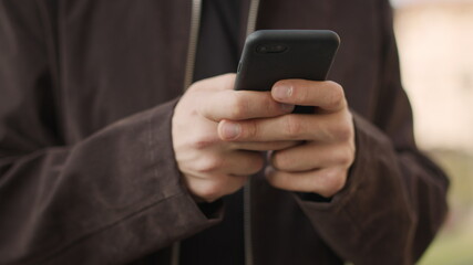 Male hands using mobile phone outdoors. Unknown guy texting phone outside