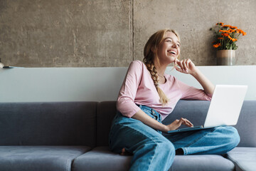 Photo of woman smiling and using laptop while sitting on couch