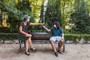 Young man and woman with mask sharing food sitting in urban park, maintaining social distance to prevent the spread of the coronavirus in Spain. Selective focus.