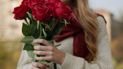 Woman hands bringing roses to face. Cheerful girl smelling flowers outdoors