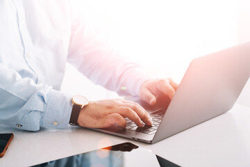 Closeup view of corporate entrepreneur working on laptop computer at table in bright interior. Male hands keyboarding text message on modern netbook.Businessman shopping online on market website on pc
