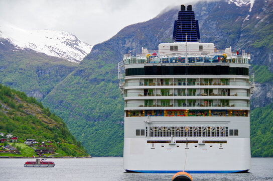 Rear view of stern of modern cruiseship or cruise ship liner and tender in Geirangerfjord Norway with breathtaking and beautiful nature and mountain landscape scenery in background in Europe&acute;s Alaska