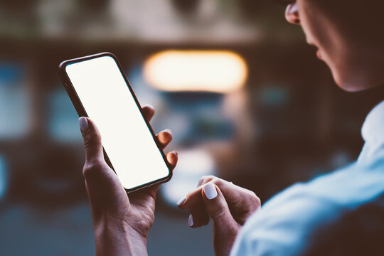 Woman's hands holding mobile phone with lighted big copy space touch screen outdoors with evening bokeh light of city. Close up view of female person using smartphone app for online shopping