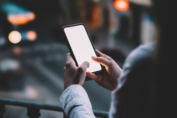 Woman's hands holding mobile phone with lighted big copy space touch screen outdoors with evening bokeh light of city. Close up view of female person using smartphone app for online shopping