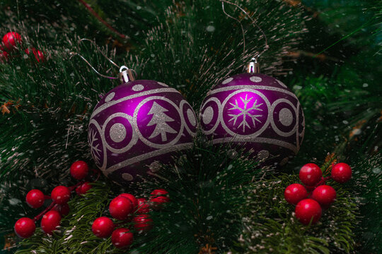 Two purple festive balloons with the image of a Christmas tree and snowflakes hanging on artificial branches of a spruce