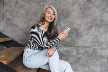 Photo of happy adult asian woman smiling and using cellphone