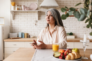 Pleased optimistic mature woman using mobile phone.