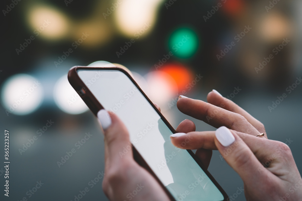 Poster cropped view of female fingers typing text message on blank display of modern smartphone on bokeh ba