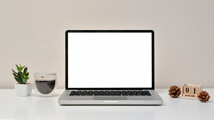 Modern workspace with blank screen laptop, coffee cup and calendar on white background. Front view. Happy new year day.