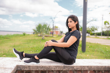 Mulher jovem e bonita sentada descansando depois da corrida e olhando para o horizonte.