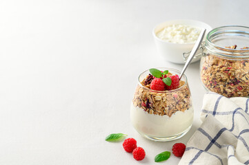 Parfait yogurt with granola and raspberries in a glass, light background, copy space. Healthy breakfast concept.