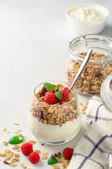 Parfait yogurt with granola and raspberries in a glass, light background, copy space. Healthy breakfast concept.