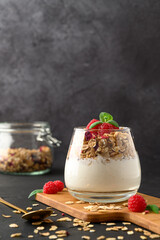 Parfait yogurt with granola and raspberries in a glass, black background, copy space. Healthy breakfast concept.