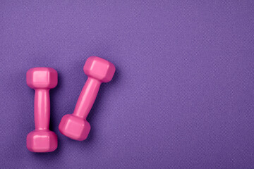 Fitness concept. Weight loss. Pink dumbbells isolated on purple yoga mat. With copy space for text