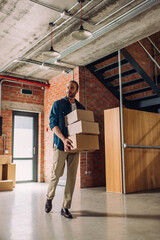 handsome businessman holding boxes and walking in new and modern office