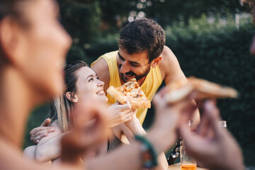 Young couple sitting on park bench and eating pizza.