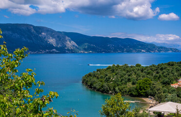Beautiful summer landscape with sea bay with calm water, village and mountains on the horizon and clouds on blue sky.