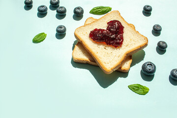 Morning breakfast bread with jam in the shape of a heart and blueberries on a blue background. Trend contrasting shadows