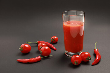 Close up view of tomato juice in glass with cherry tomatoes and red chili pepper isolated on black...
