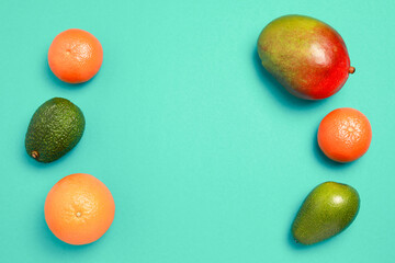 Close up macro top view of resh mix  tropical fruits. Mango, oranges and avocado isolated on green background with copy space.
