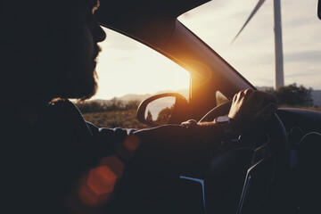 Young bearded hipster guy sitting behind the wheel of rented car during his anticipated travel on...