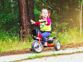 Little kid riding a tricycle on a sunny summer day in the meadow