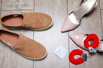 Man shoes and woman heels with condom and red sex toy handcuffs in the middle. A concept of having safe sex.