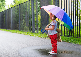 A little girl stands under an umbrella and looks into the distance.
