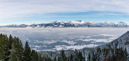 Amazing panoramic View to snowy Mountain Range above foggy cloud layer. View from Rangiswangerhorn to Illertal, Allgau, Bavaria, Germany.
