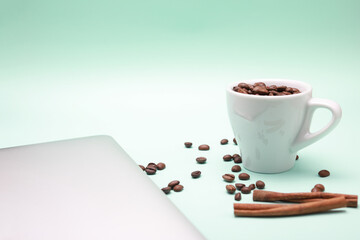 Cup of coffee, beans, and laptop isolated on a light green background.