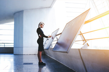 Beautiful female reading advertising about a project on interactive computer display while standing in office interior, businesswoman searching information on high tech modern device