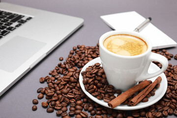 Cup of coffee with beans inside and laptop isolated on wooden background.