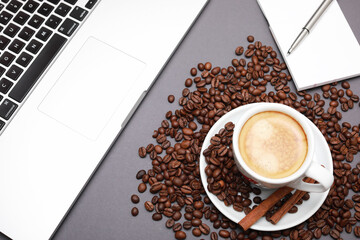 Cup of coffee with beans inside and laptop isolated on wooden background.