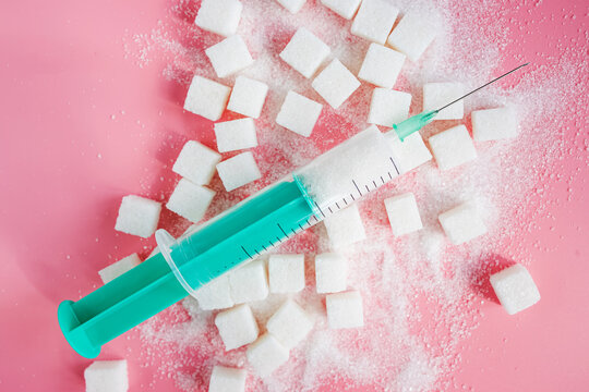 Granulated sugar, sugar cubes and syringe on pink backgroud.