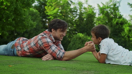 Father and son lying on grass in field. Man and boy competing in arm wrestling