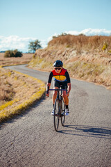 Obraz premium Female professional cyclist quickly descends the slope of a beautiful countryside road on a sunny blue sky day.