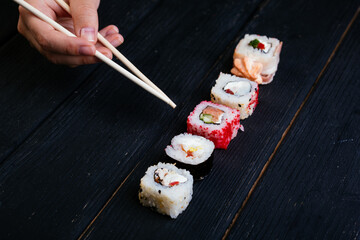Female hand takes chopsticks sushi rolls with Chinese chopsticks. Lying on a black wooden board. View from above