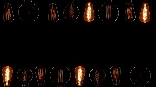 A lot of Edison bulbs creating great background for logo or title. Blinking lamps black background isolated. Vintage lights turn on and off. Yellow light amber color comes from old dirty lamps.