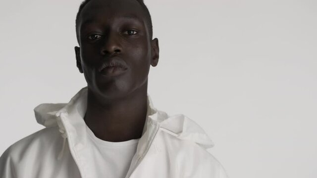 Close up handsome serious African American guy in white jacket confidently posing on camera over gray background