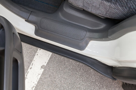 Close-up of a car running board with an open door with a gray plastic trim on the threshold of a white Japanese crossover after pre-sale preparation.