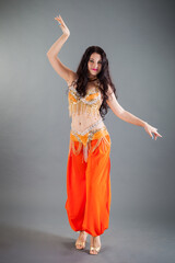 long dark hair girl in orange belly dancer costume poses at camera in studio