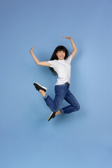 Jumping high, looks emotional, happy, cheerful. Portrait of young asian woman isolated on blue background. Beautiful cute girl. Human emotions, facial expression, sales, ad, online shopping concept.