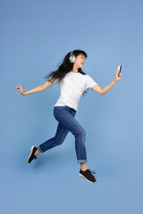 Jumping high with card and smartphone. Portrait of young asian woman isolated on blue background. Beautiful cute girl. Human emotions, facial expression, sales, ad, online shopping concept.
